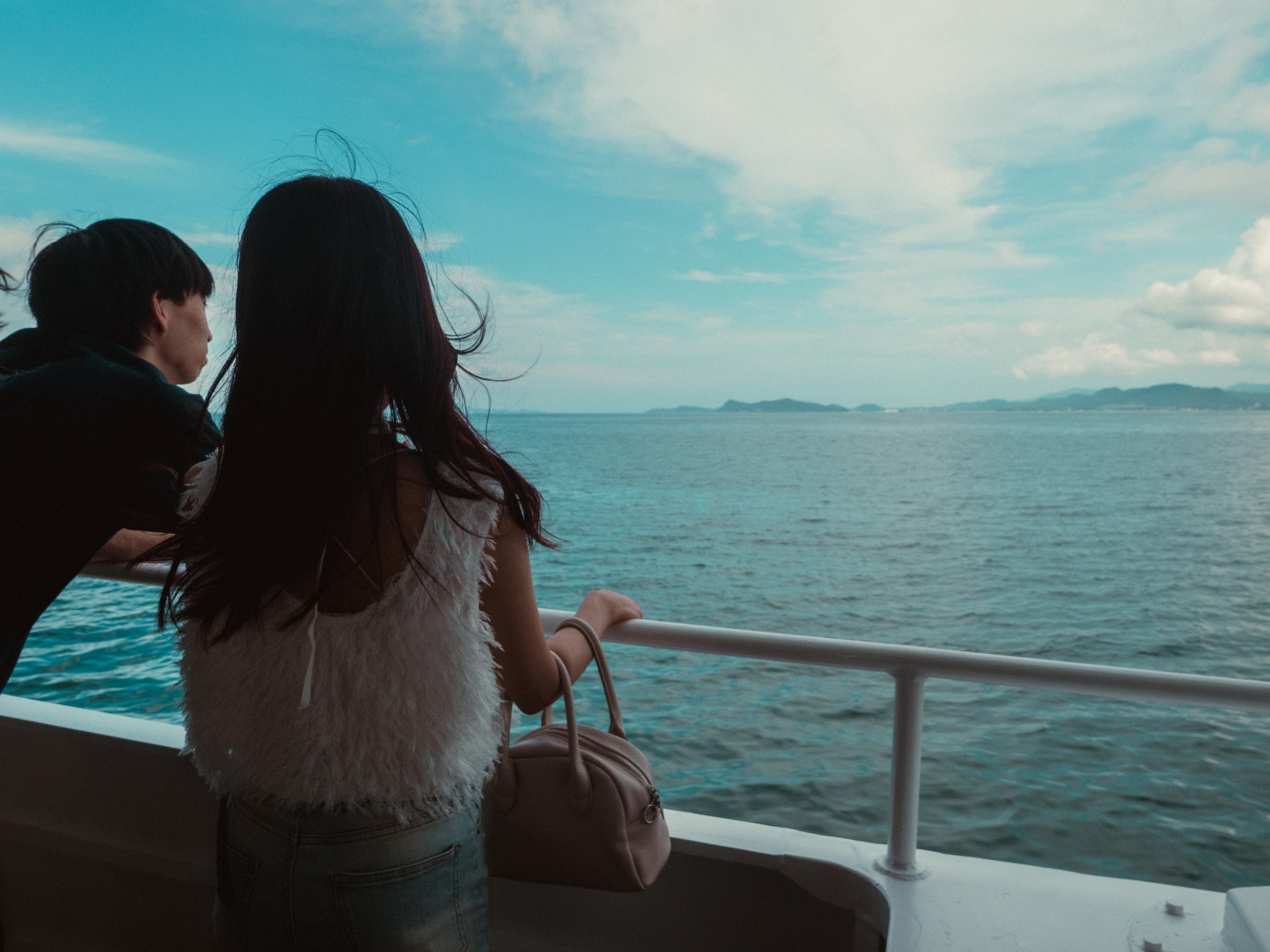 Two passengers looking out from a ferry toward islands in the sea