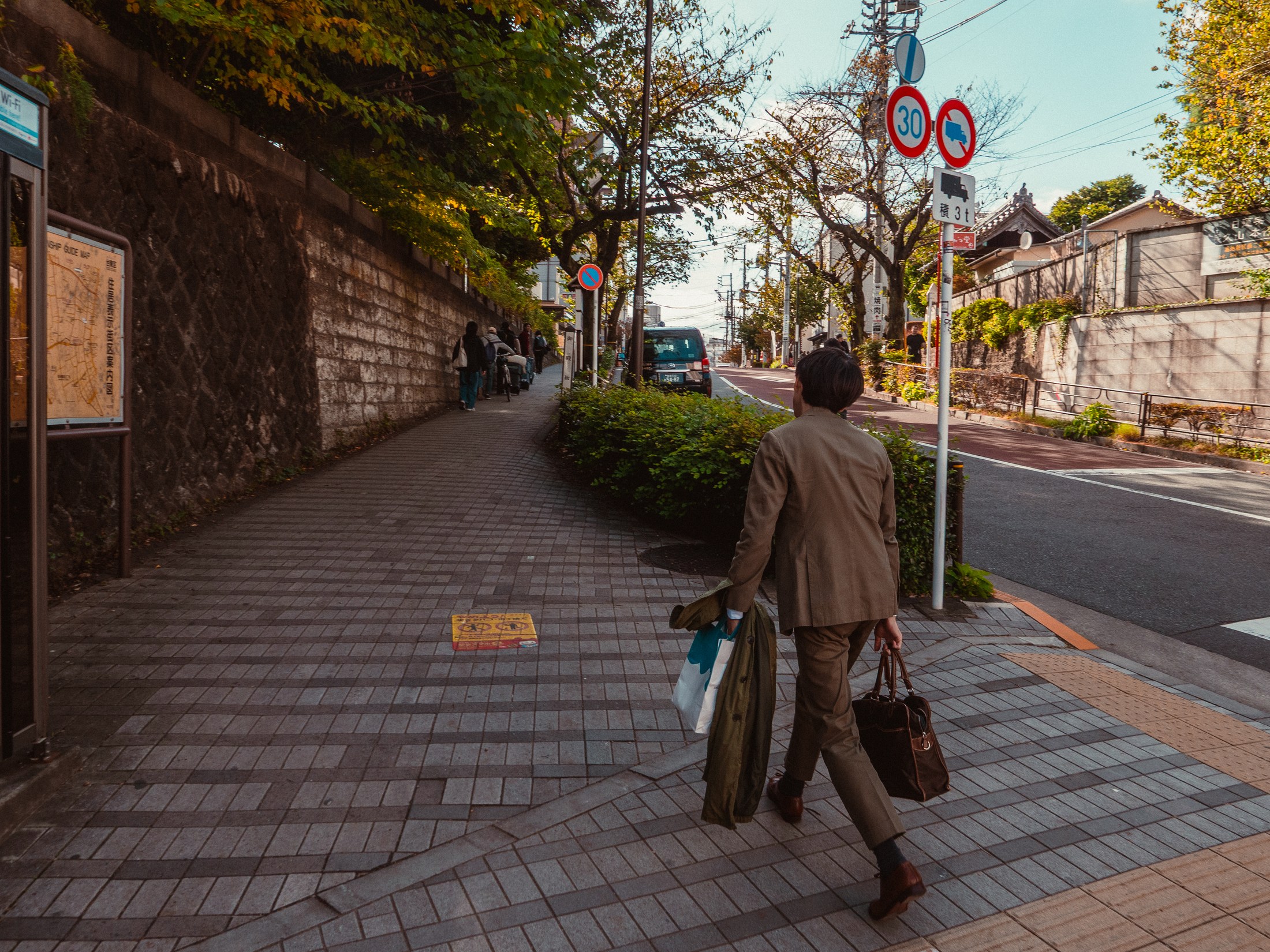 A suited man carrying bags along a sunlit street in Japan